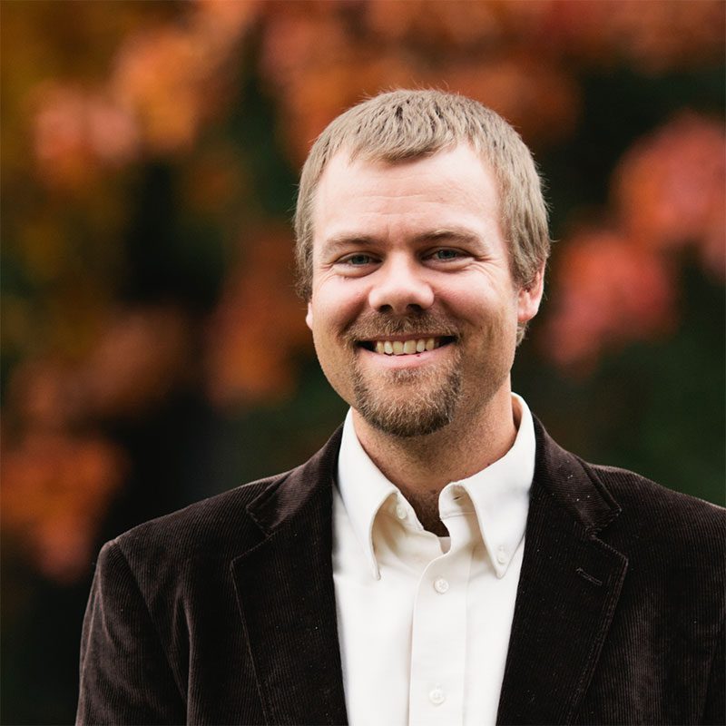 Brian Reitnour wearing brown blazer standing outside on a fall day.