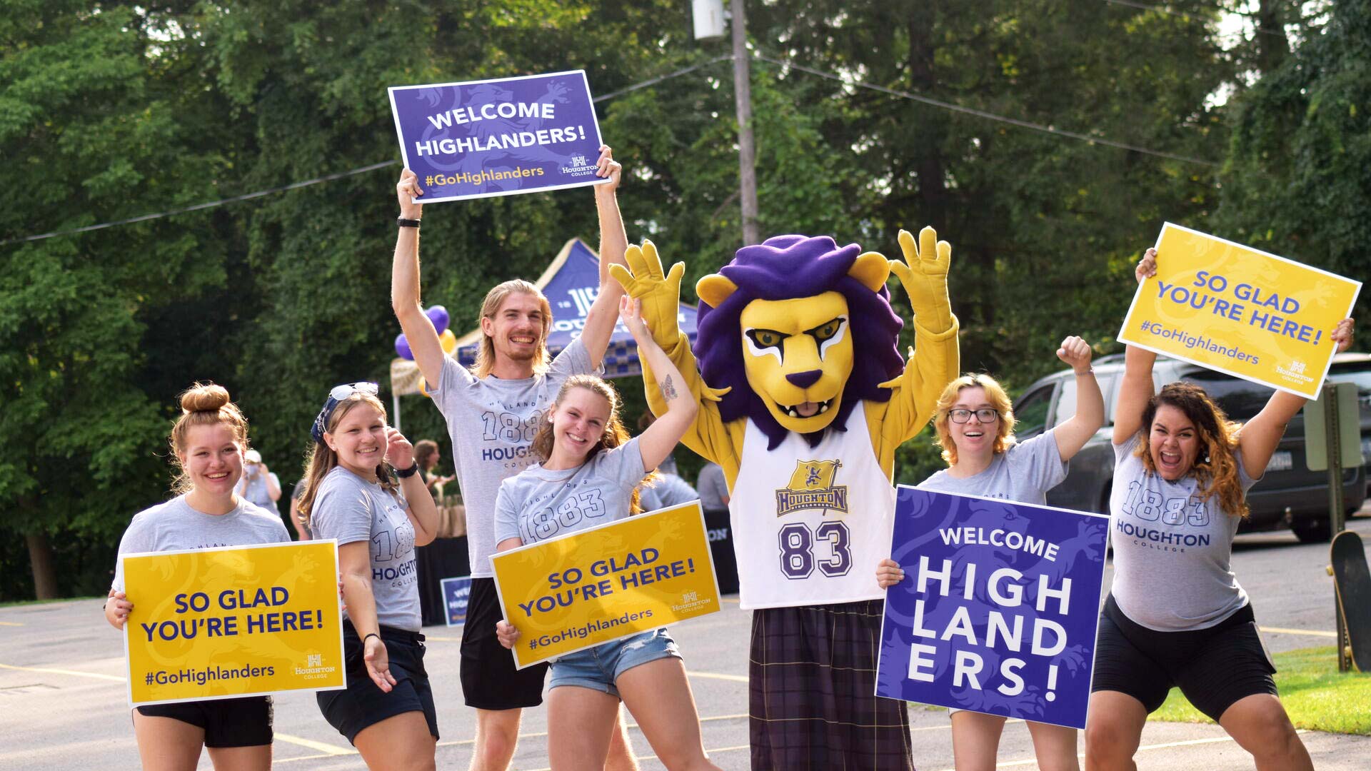 students with Luckey the Lion holding signs and shouting to welcome new students to campus
