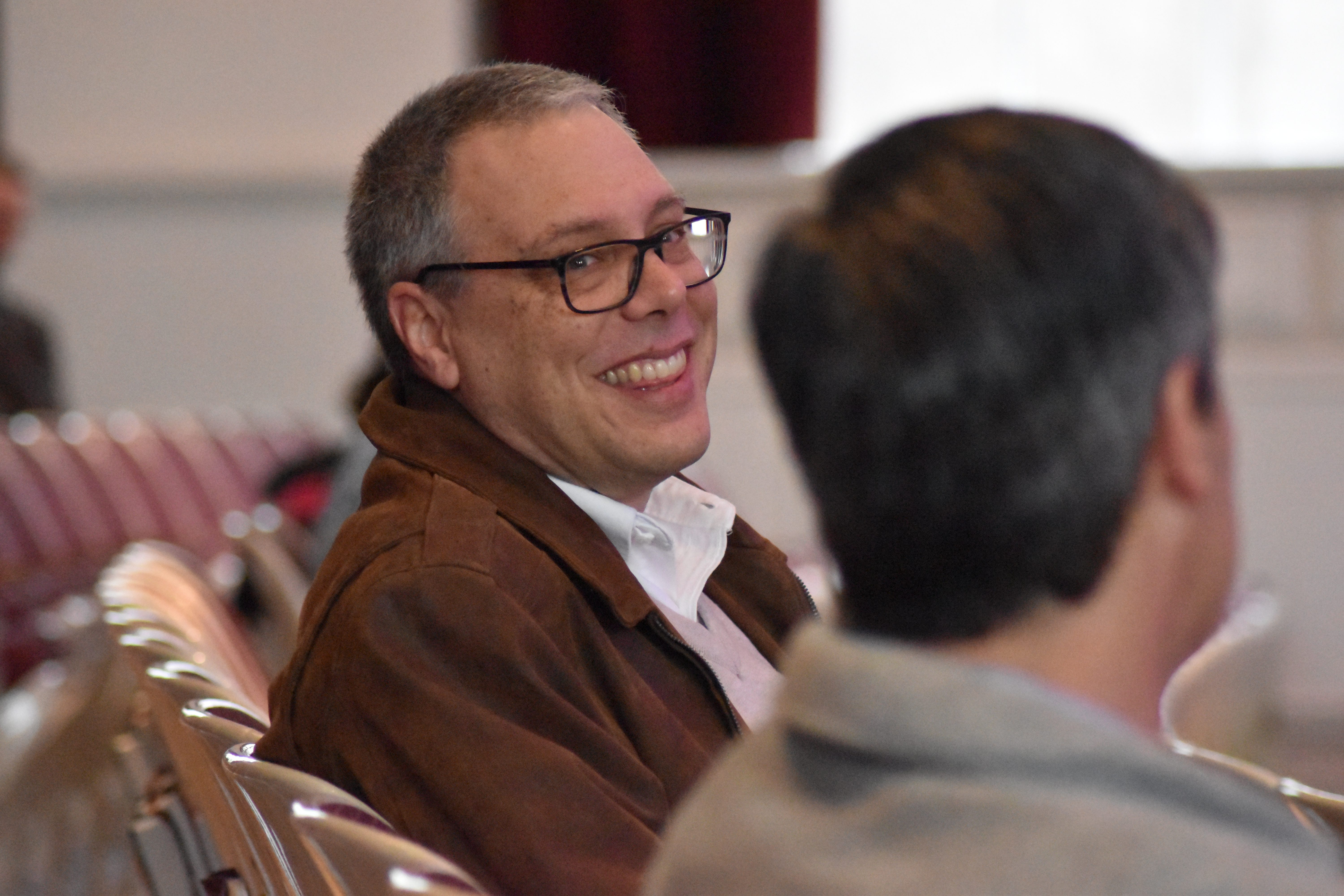 Man sitting in audience smiling and turning to talk.