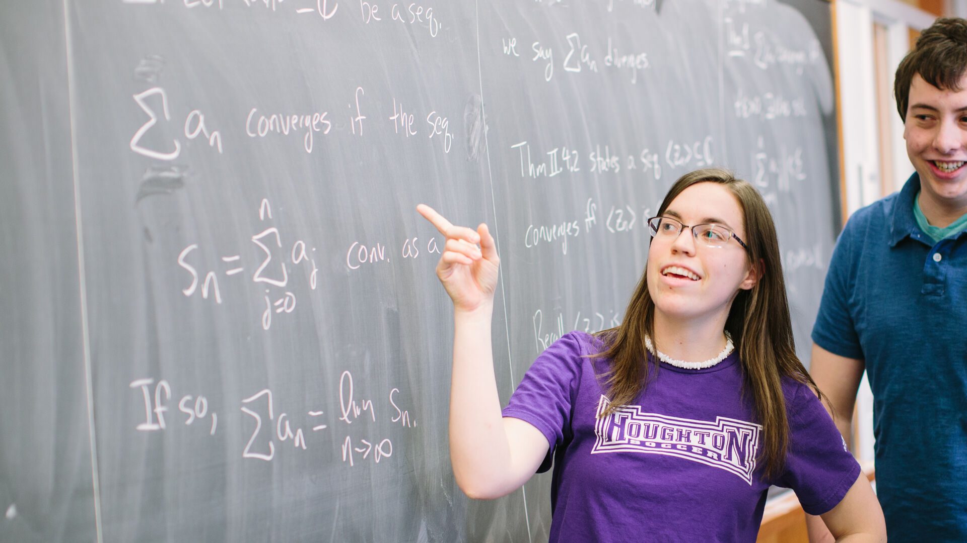 Houghton Universitystudent working through equation on board during math class.