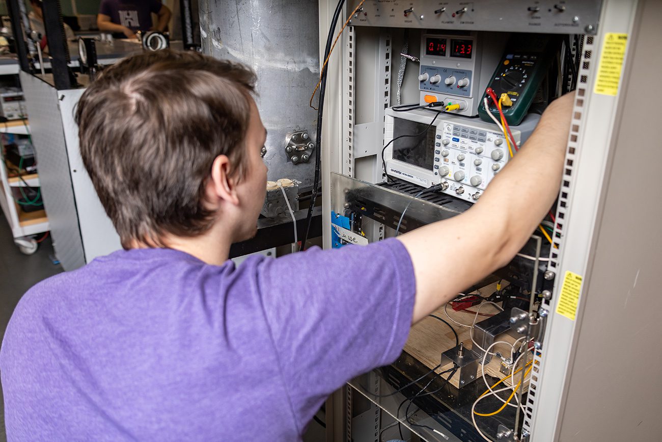 Houghton Universitystudent working with thin film deposition chamber in physics lab.