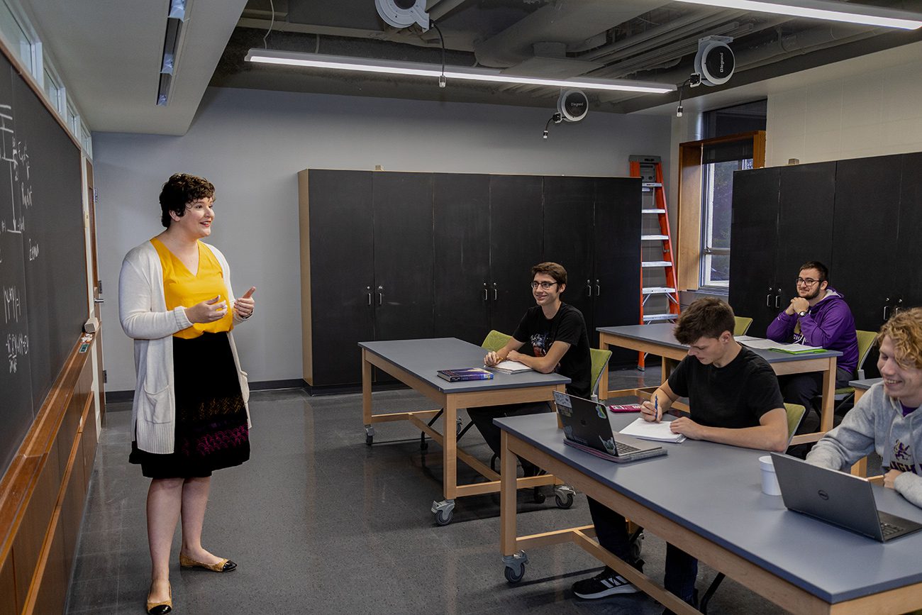 Houghton Universitystudents sitting in physics classroom listening to professor demonstration on blackboard.