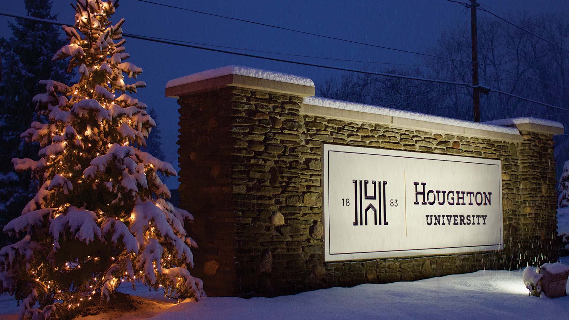 Houghton Universityscreen at night beside Christmas tree in the snow