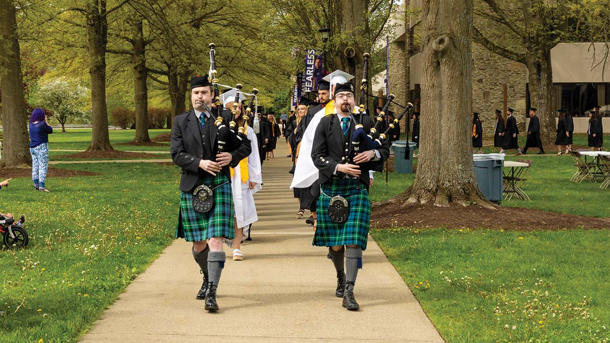 Bagpipers walking down sidewalk with graduating class during commencement.