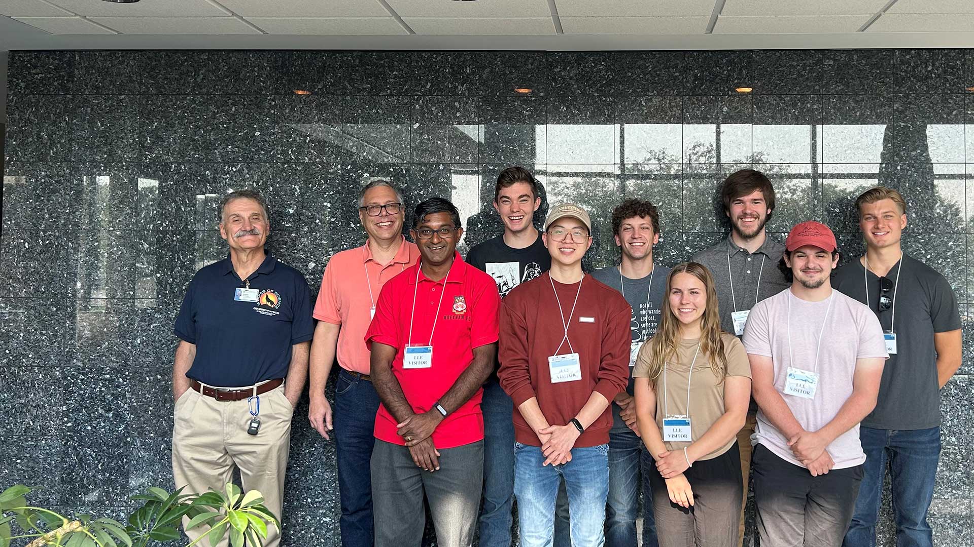 Houghton Universityphysics students and professors standing in front of granite wall at Laser Laboratory.