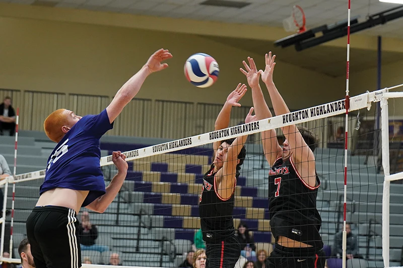 Houghton Universitymen's volleyball player hitting ball over net to opponents.