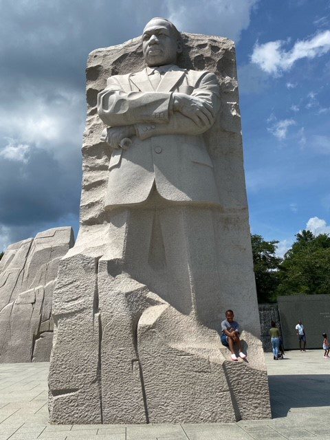 Houghton President Wayne Lewis's daughter sitting next to a large stone carved Martin Luther King Jr. statue.
