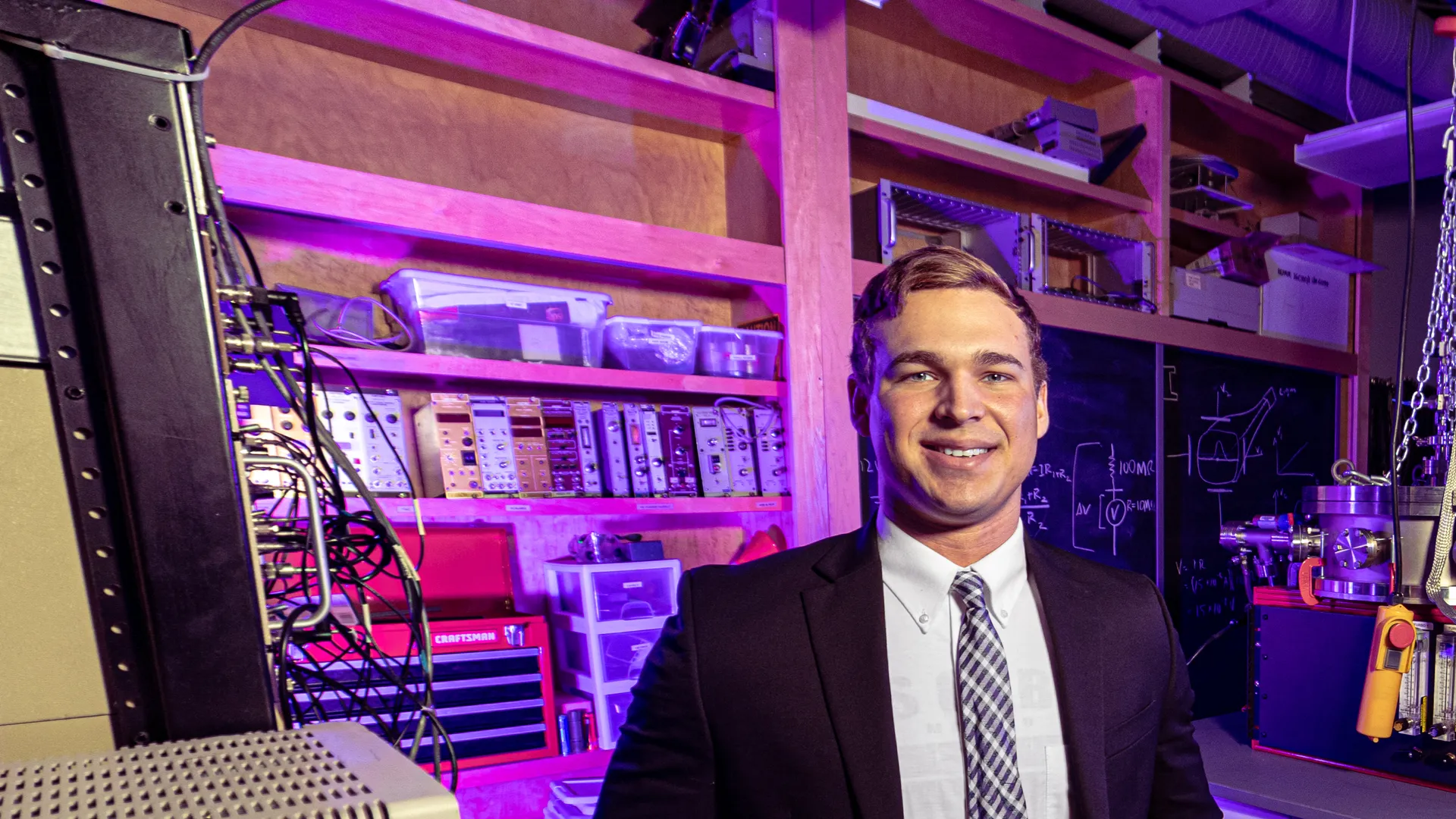 Houghton Universityrecent alumnus Malachi Yeager standing in lab in front of equipment.