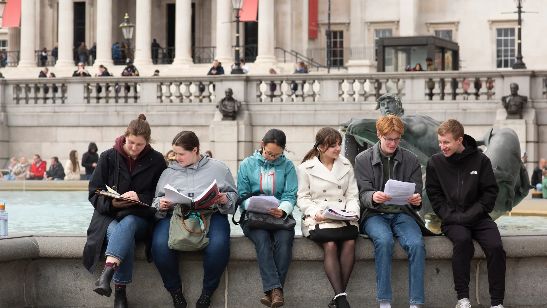 Houghton University Honors students sitting on fountain ledge looking through packets.