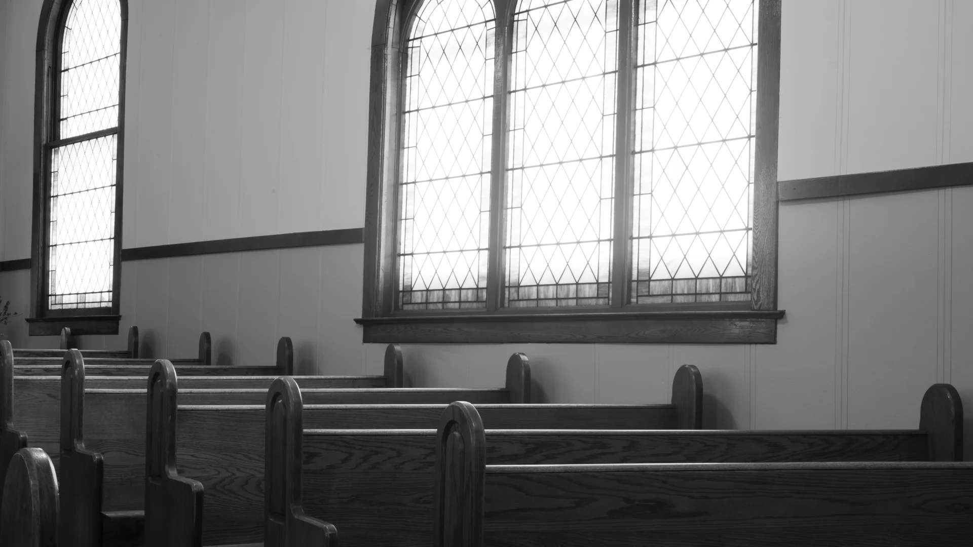 Black and white photo of sun lit windows in church.