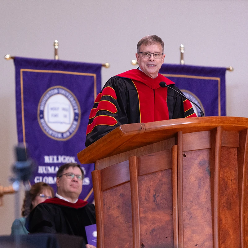 Houghton Universitycommencement speak Wayne Schmidt standing on podium in regalia.