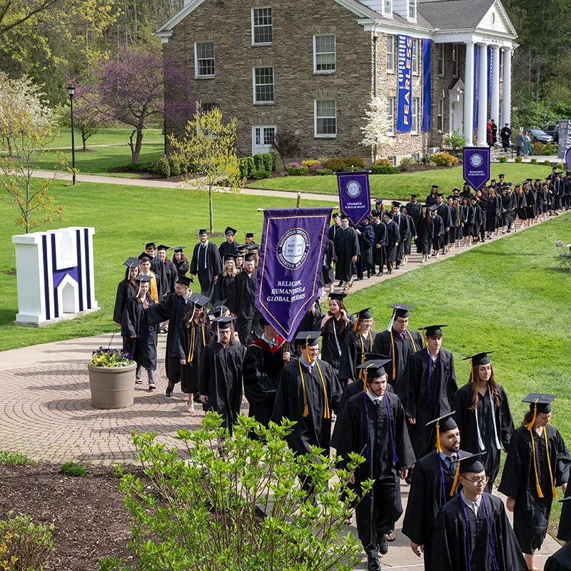 Houghton Universitygraduates walking on quad in regalia.
