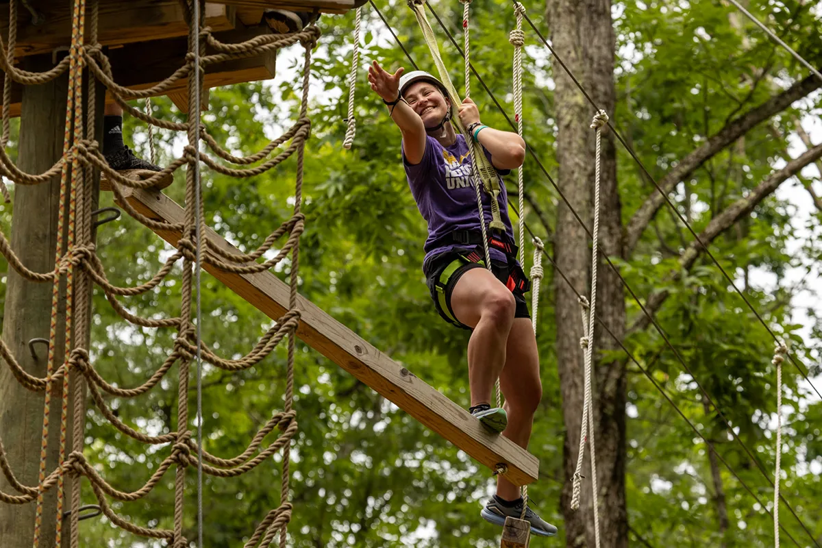 Houghton Universitystudent reaching for rope on EPIC high ropes course.