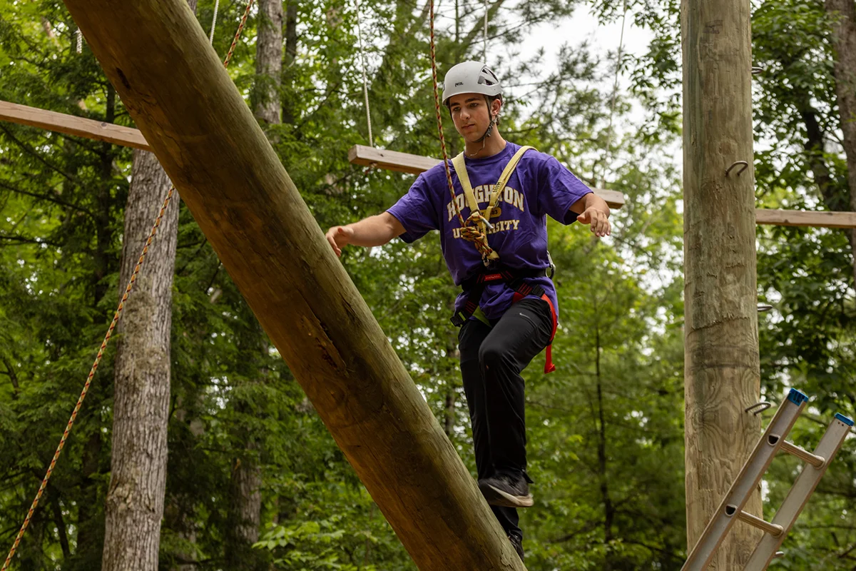 Houghton Universitystudent walking log on EPIC Adventures Ropes Course.