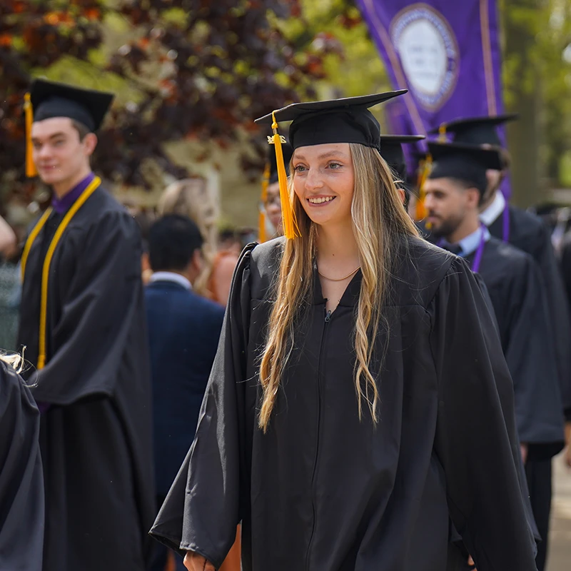 Houghton Universitygraduate walking with cap and gown.