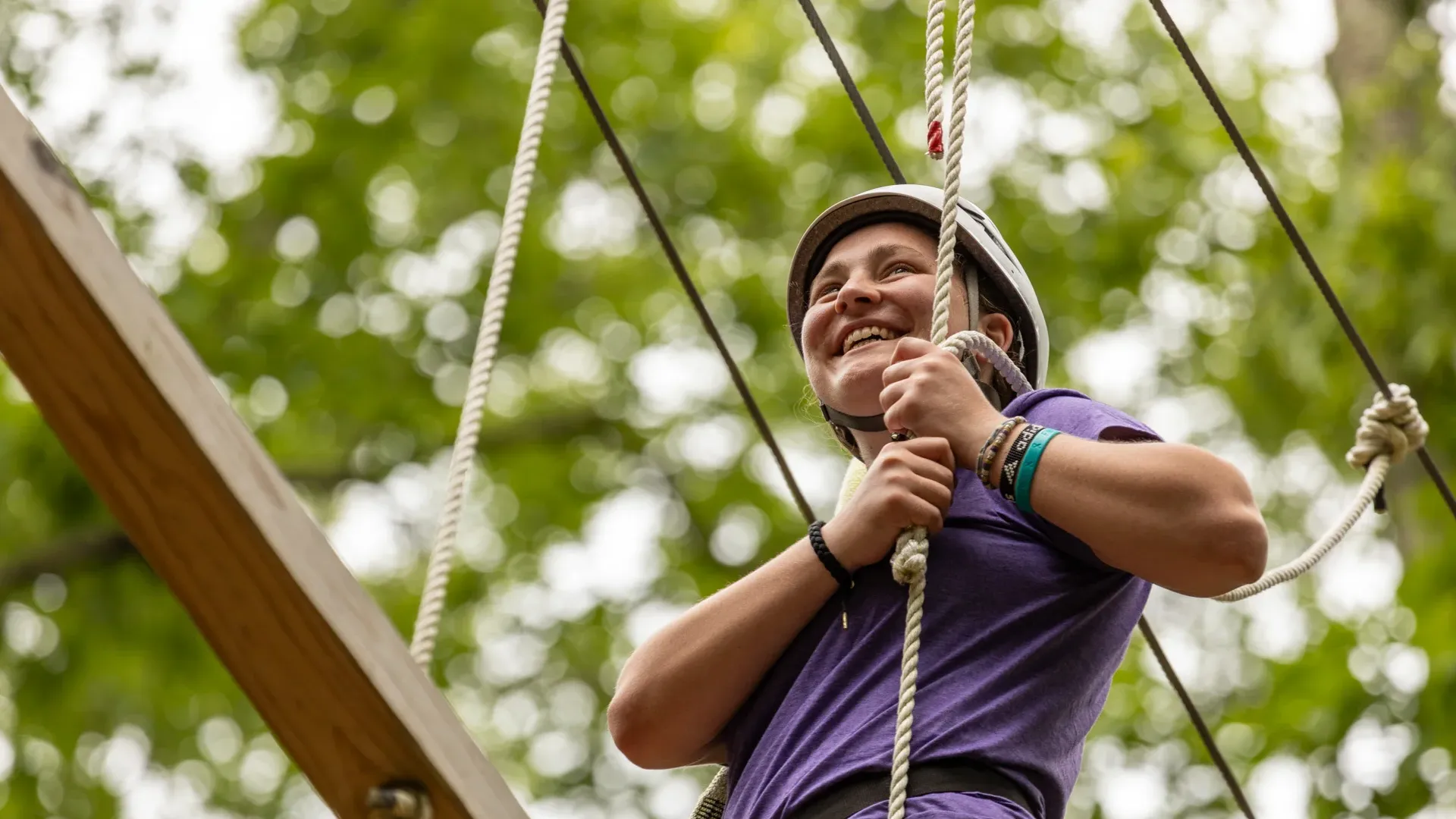 Houghton Universitystudent standing on Epic Adventures ropes course wearing purple shirt and helmet.