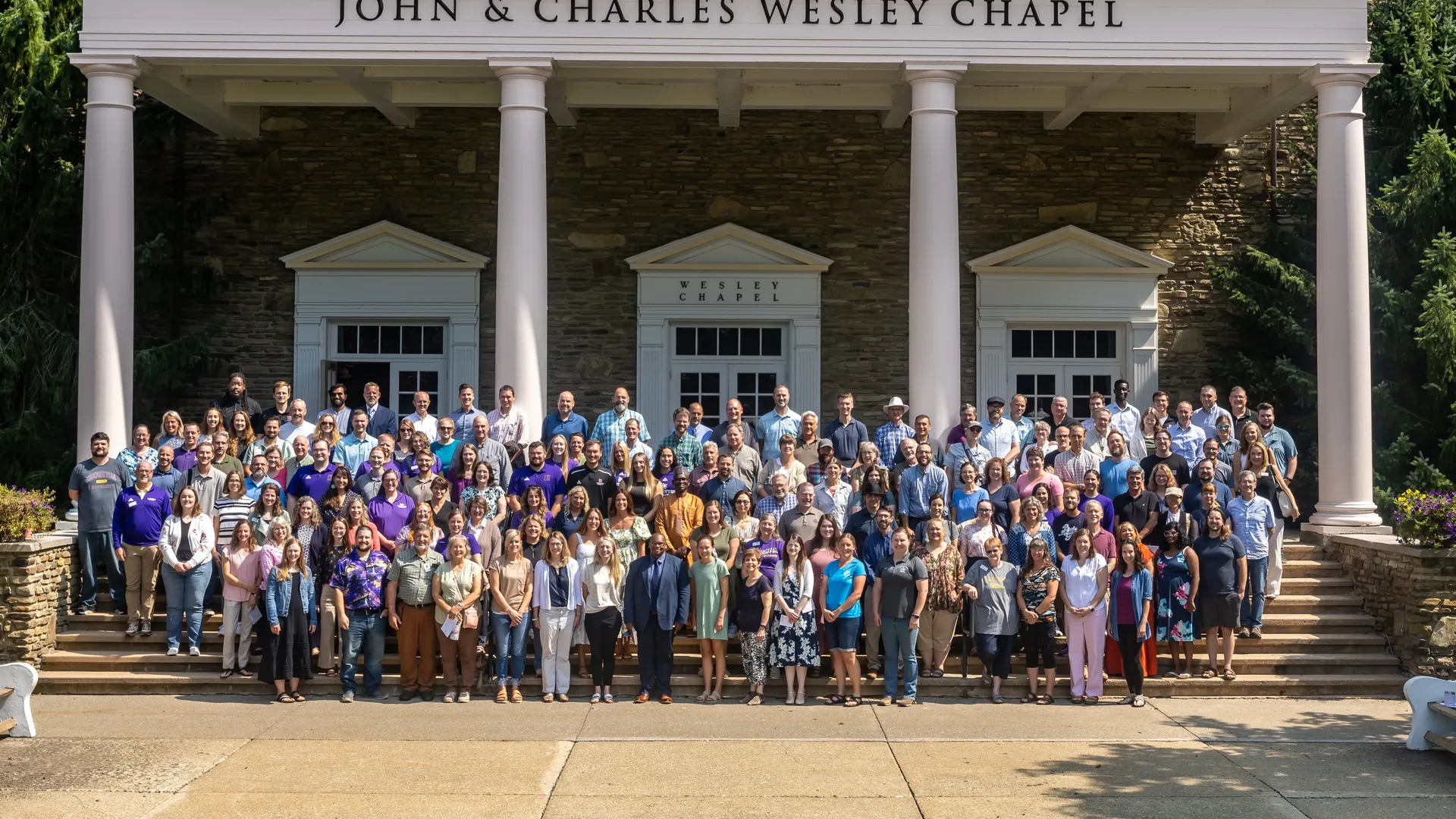 Houghton Universitystaff and faculty standing on the steps of the Wesley Chapel.