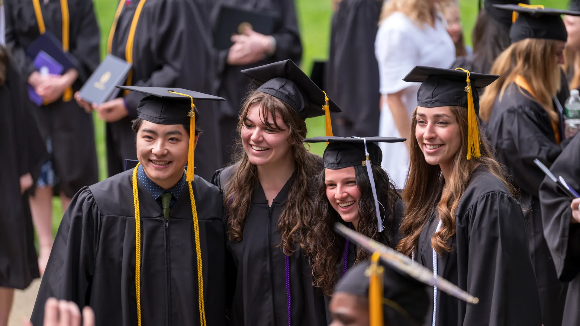 Four ����ר�� graduates standing together for picture in graduation regalia.
