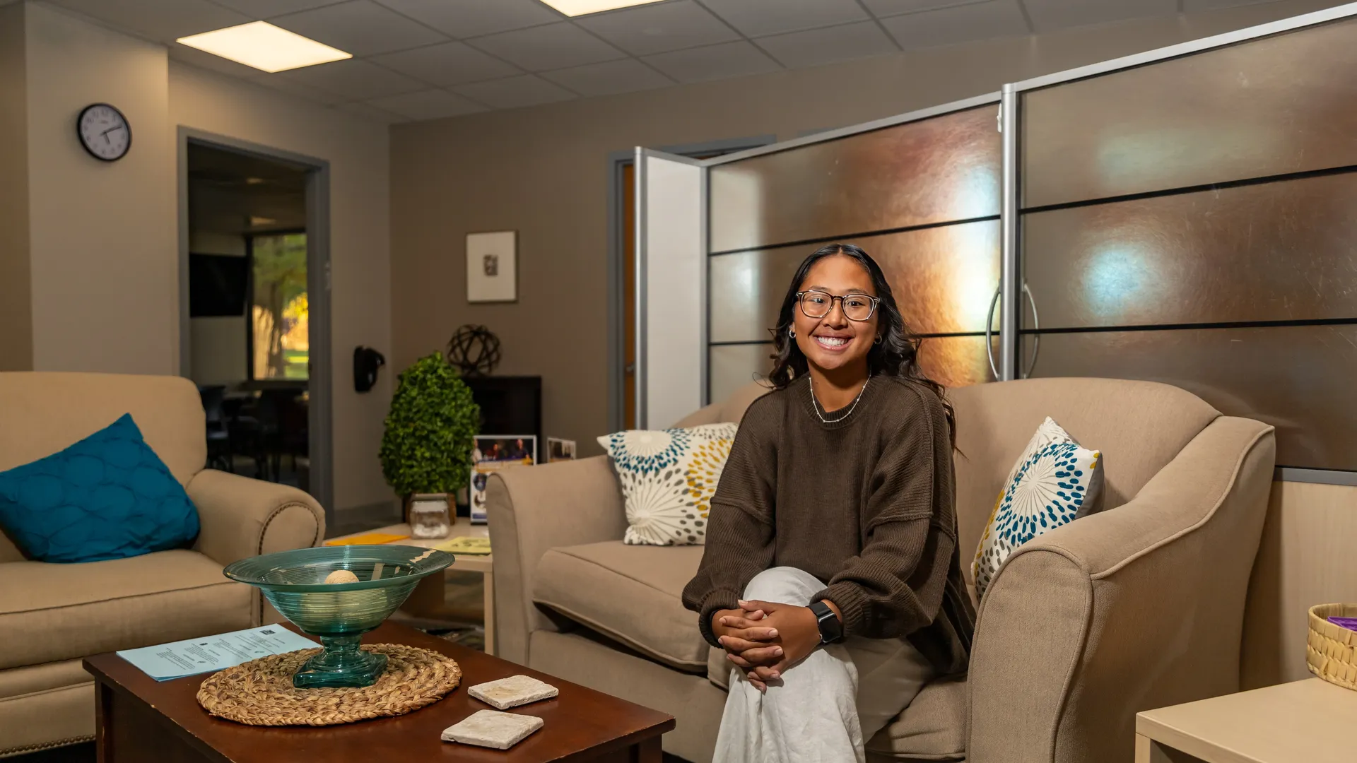Houghton Universitystudent MyaKay Bartman sitting on couch in campus office space.