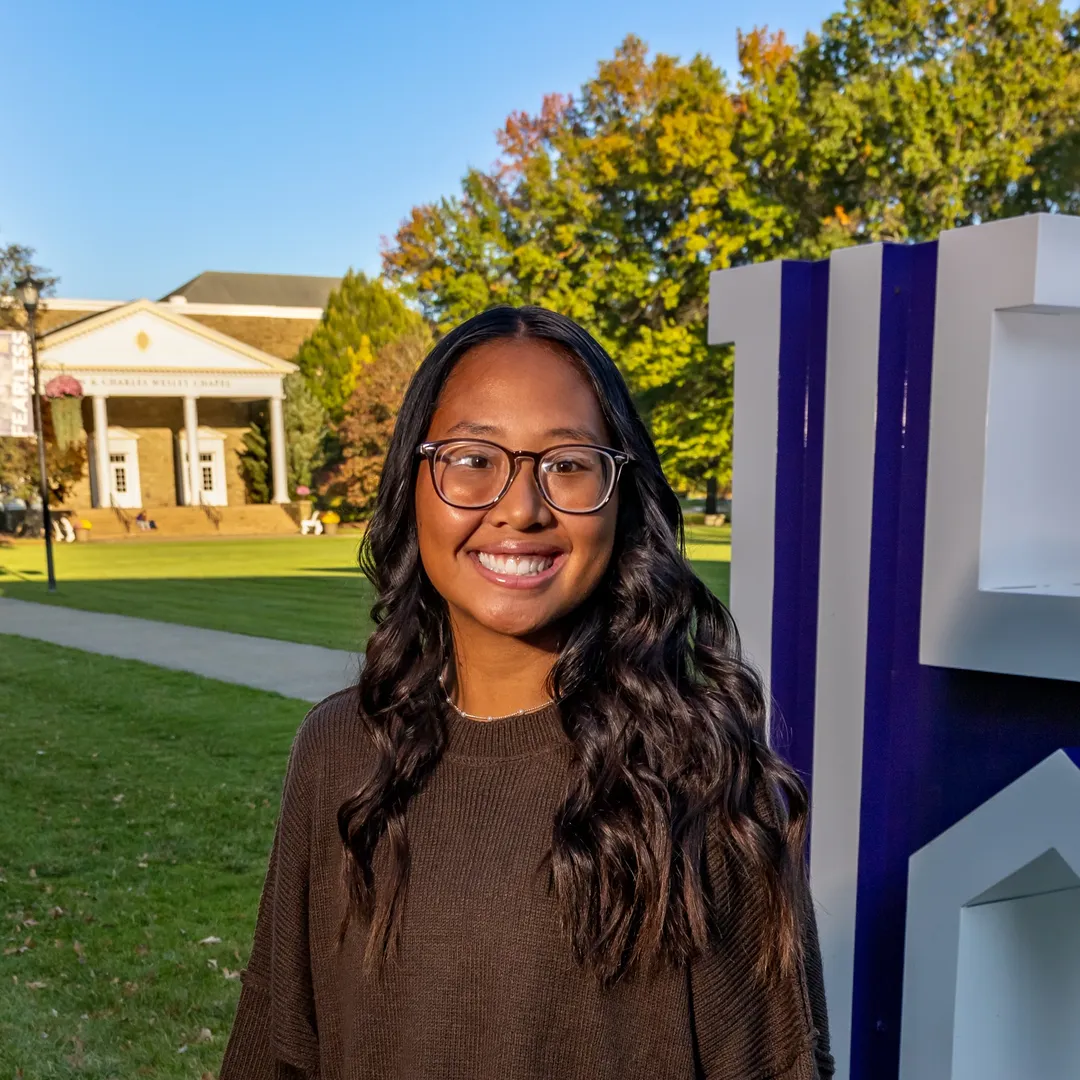 Houghton Universitystudent MyaKay Bartman standing on by H on quad during beautiful fall day.