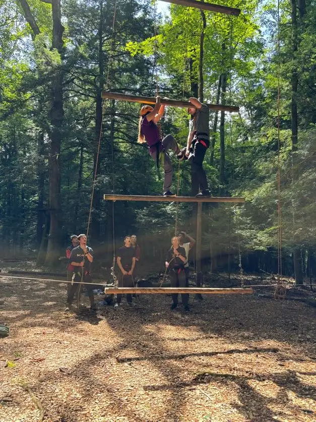 A group of student watching two other students climb ropes course ����ר��.