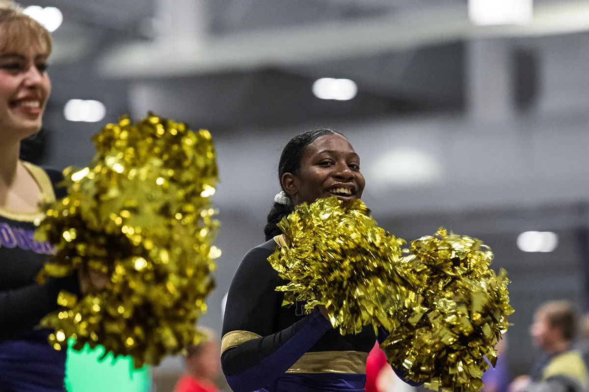 Houghton Universityclub cheerleading student with golden pom poms at Homecoming.