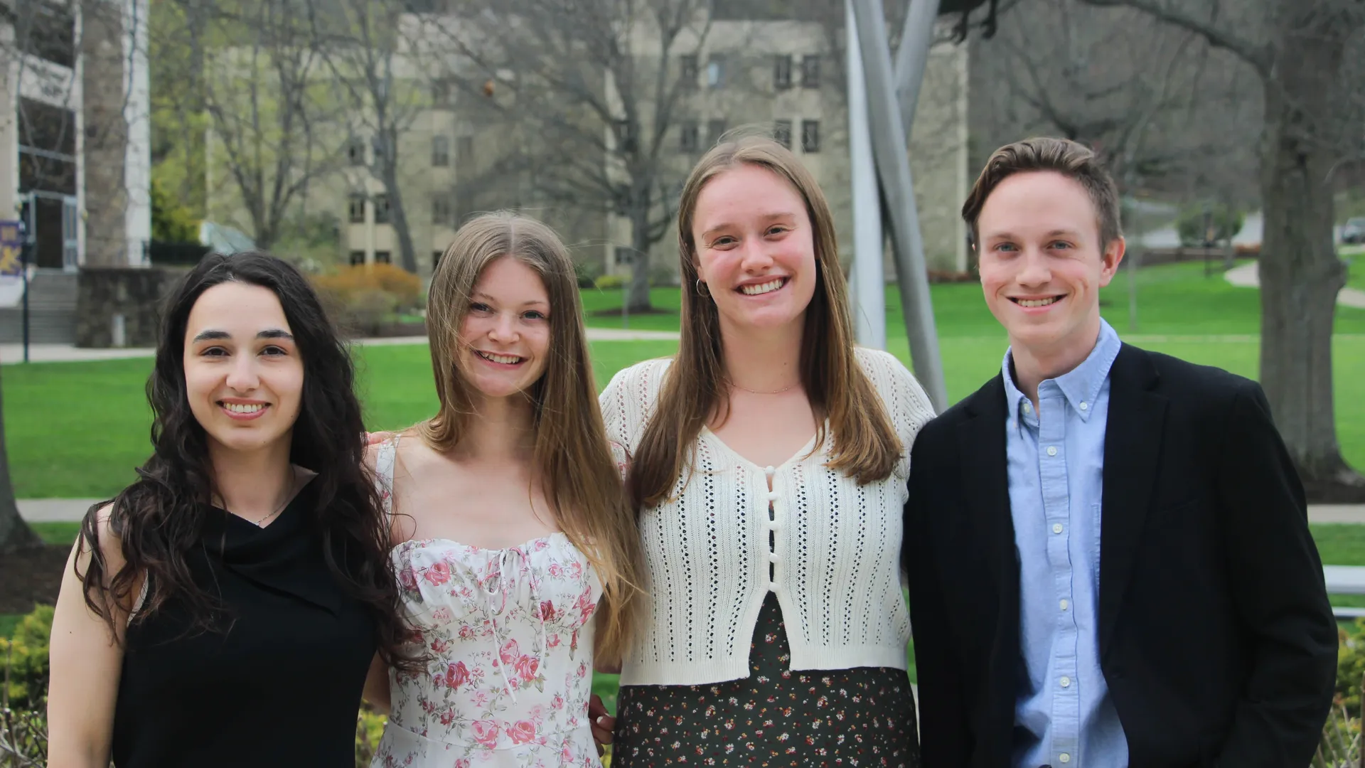 Four students of Psi Chi standing outside on the lawn smiling.