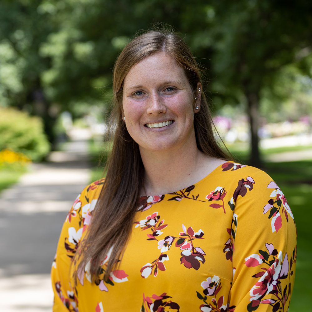Staff member Katie Govan with gold floral shirt standing on campus.
