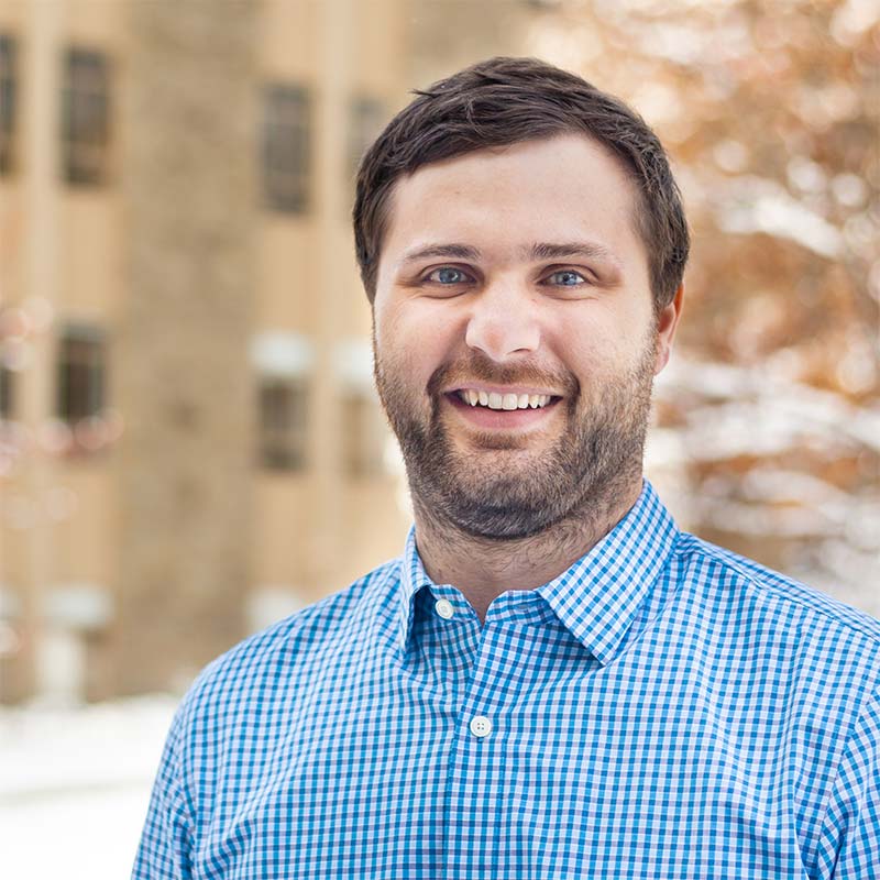 John Oden with blue checkered shirt standing outside on campus during a winter day.