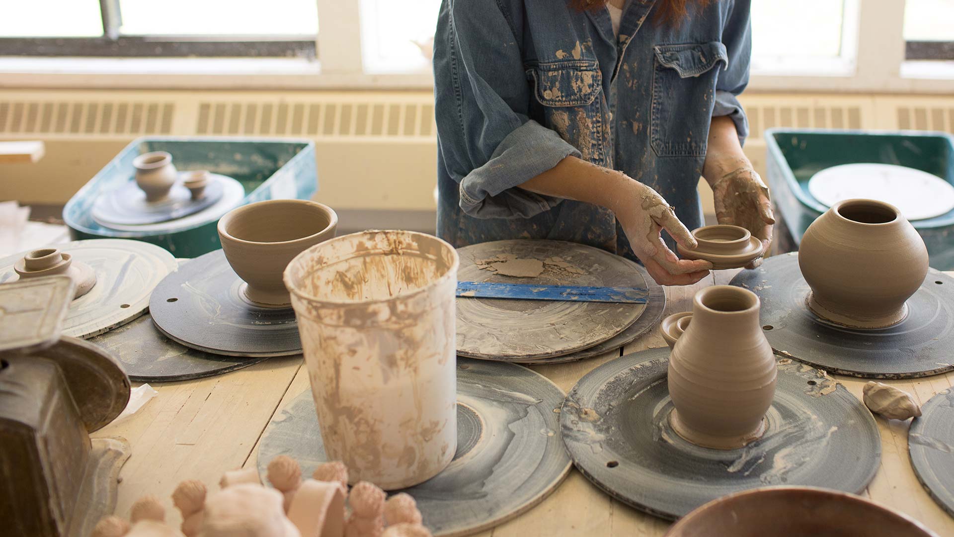 Houghton studio art major student arranging pottery on table in ceramics class.