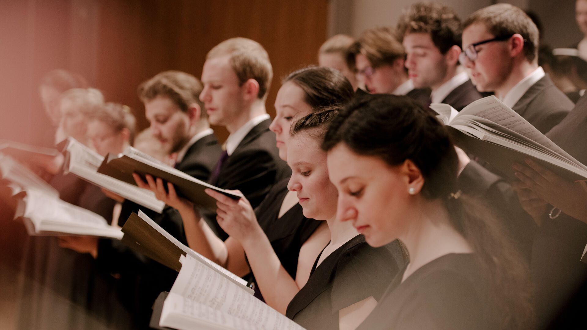 Houghton University graduate music students participating in choir holding music and singing.