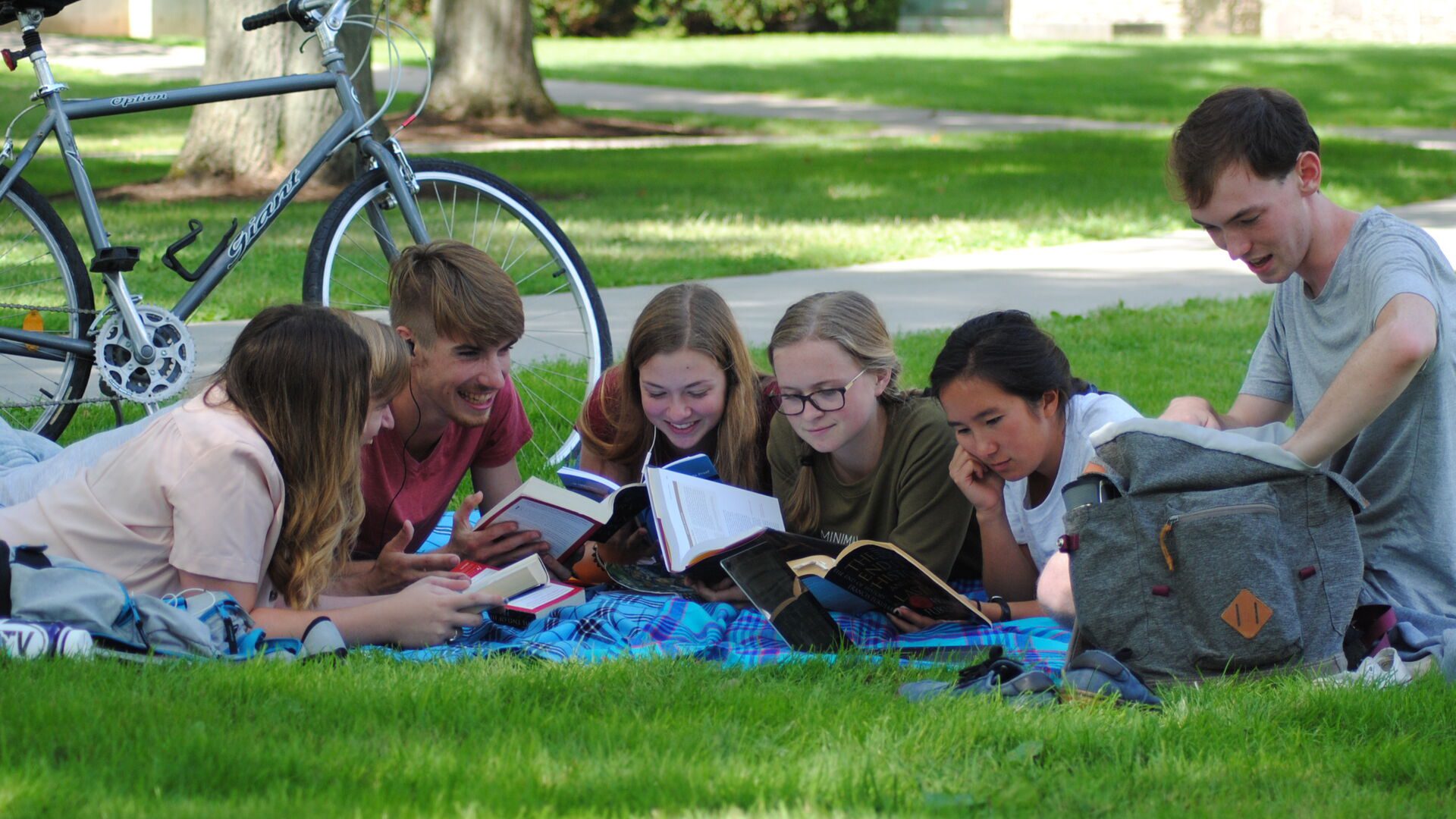 Students laying on the lawn reading a book together.