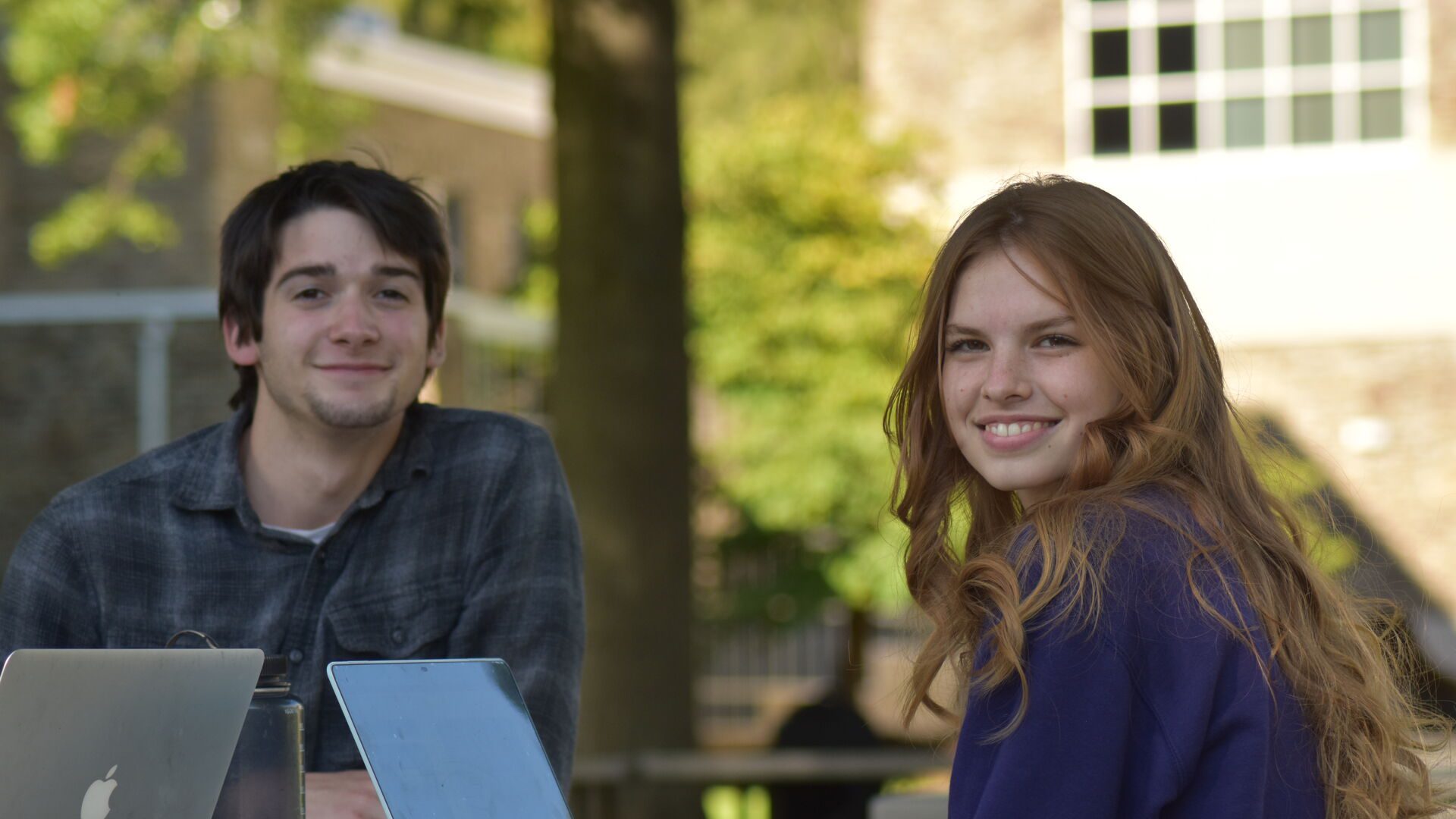 Two students sitting at table with laptops smiling
