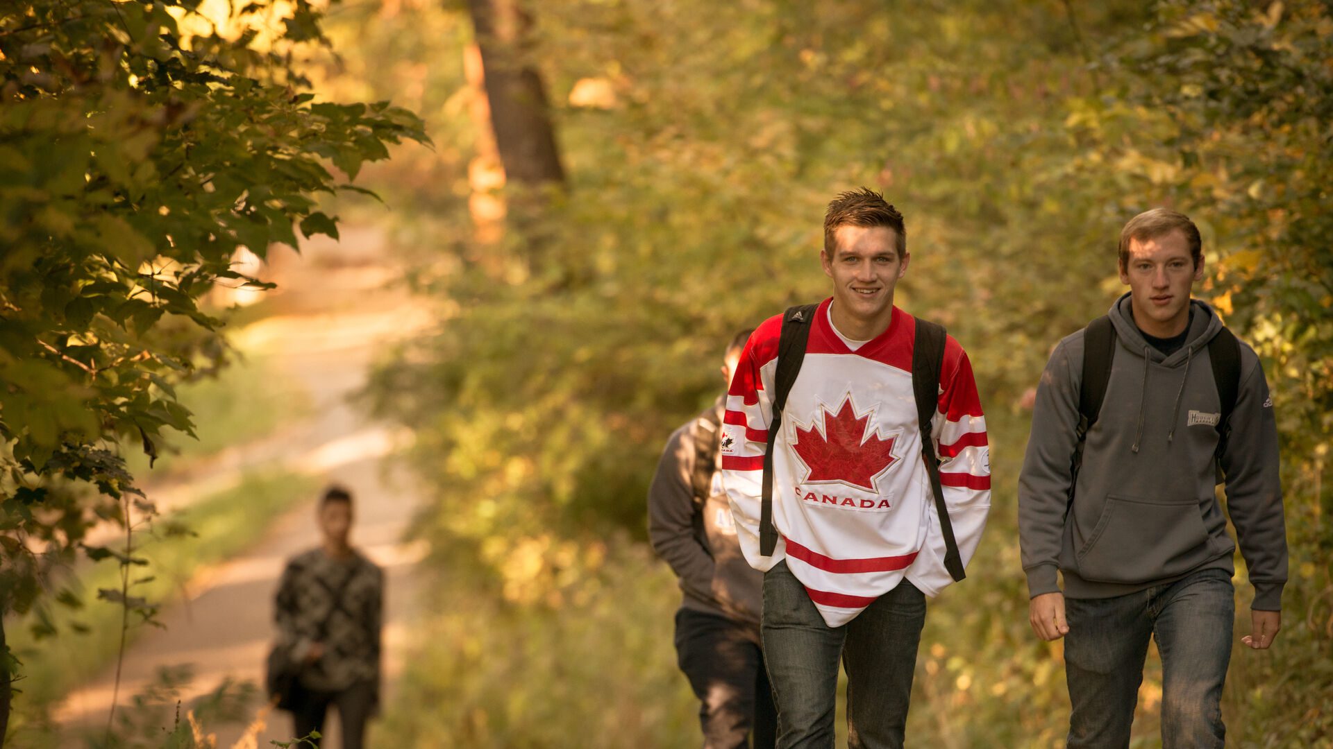 Student wearing Canadian Maple Leaf hoodie walking up path.