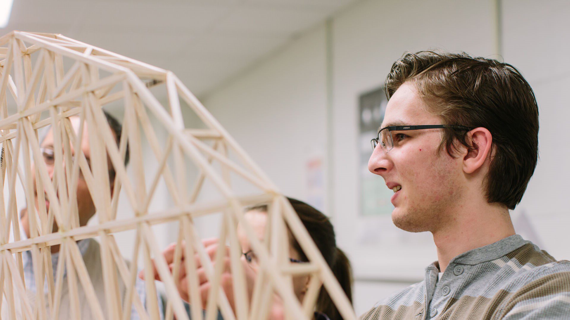 Student working on wooden bridge construction in a physics lab class.