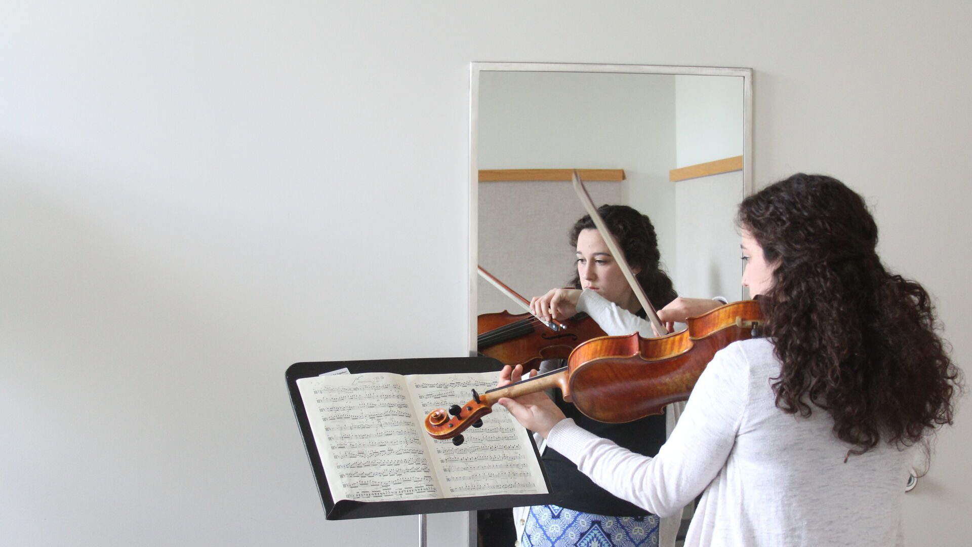 Houghton music graduate student playing her violin while looking the mirror.