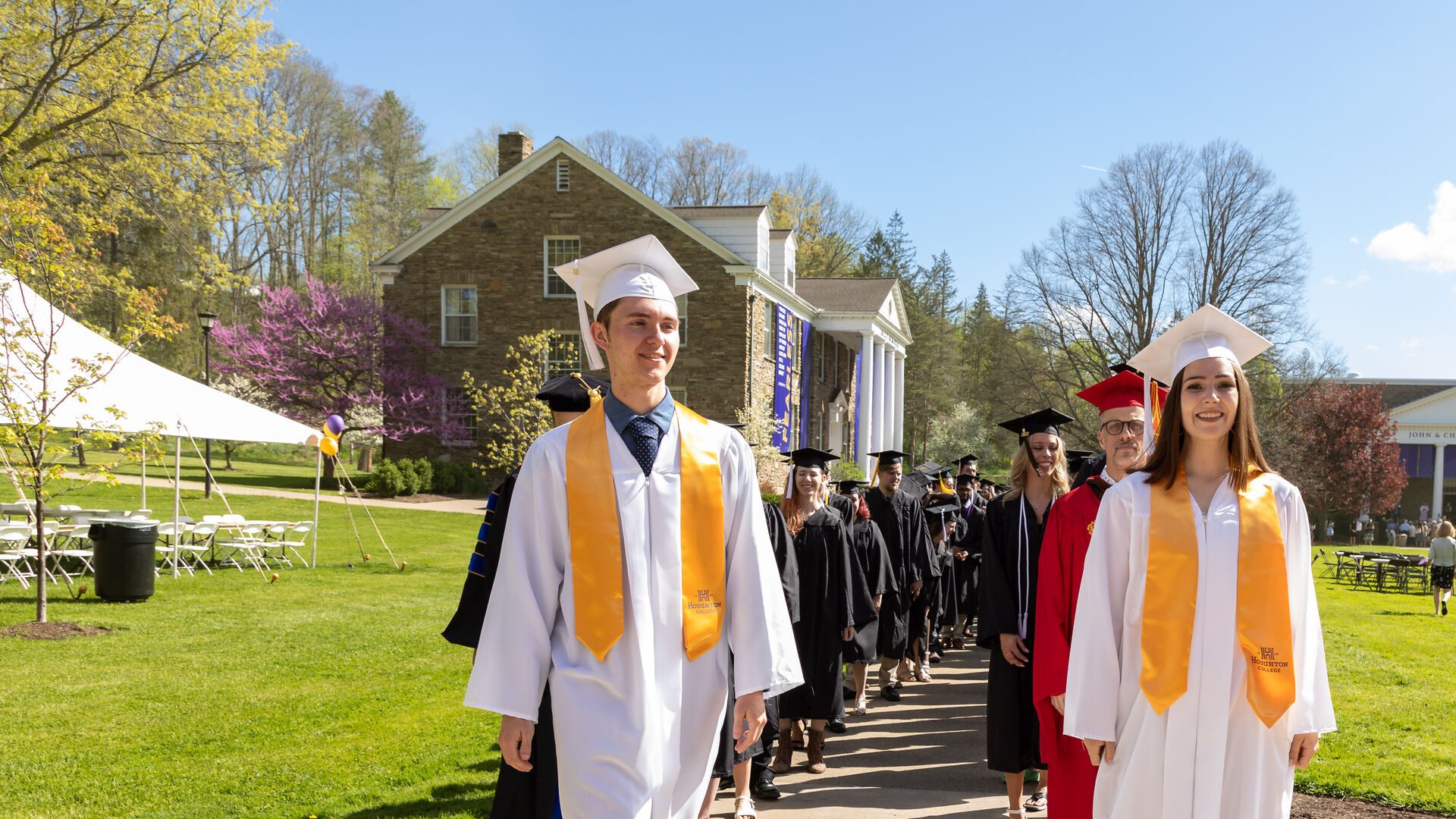 Two Houghton students leading Houghton faculty and soon to be graduates around the quad during Commencement.