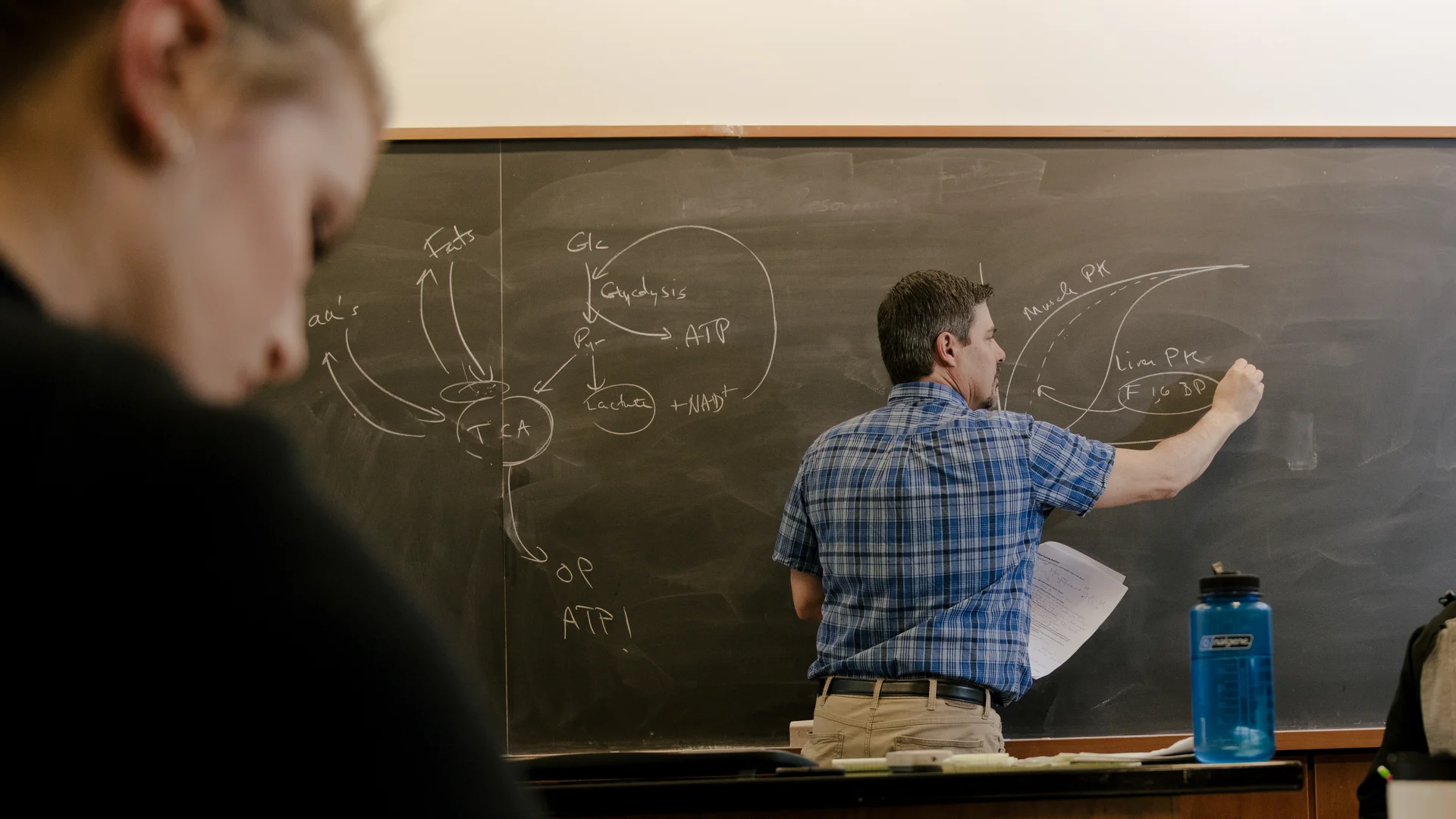 Houghton professor writing equations on blackboard during biochemistry class.