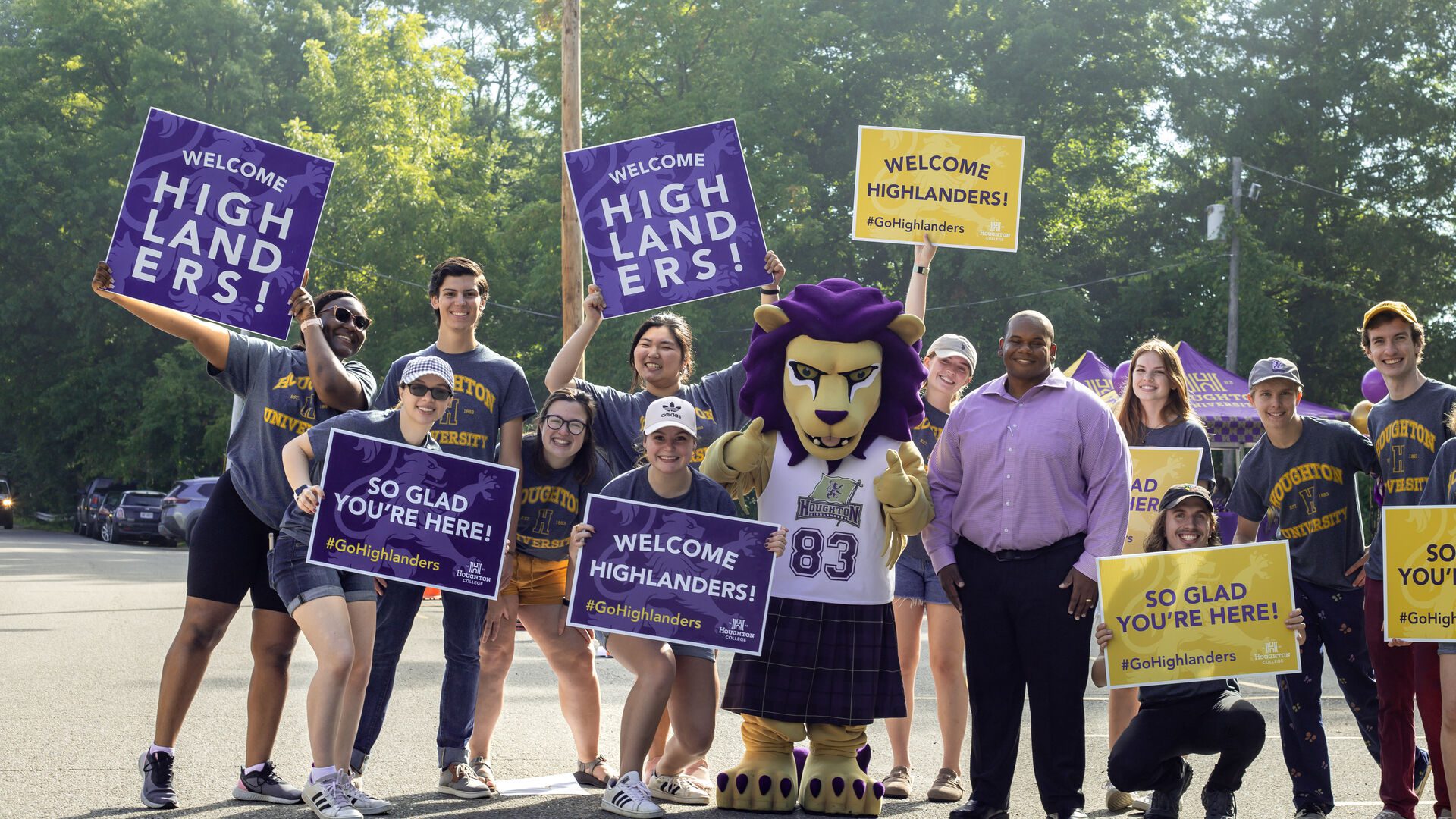 A group of Houghton students standing with President Lewis holding gold and purple welcome signs.