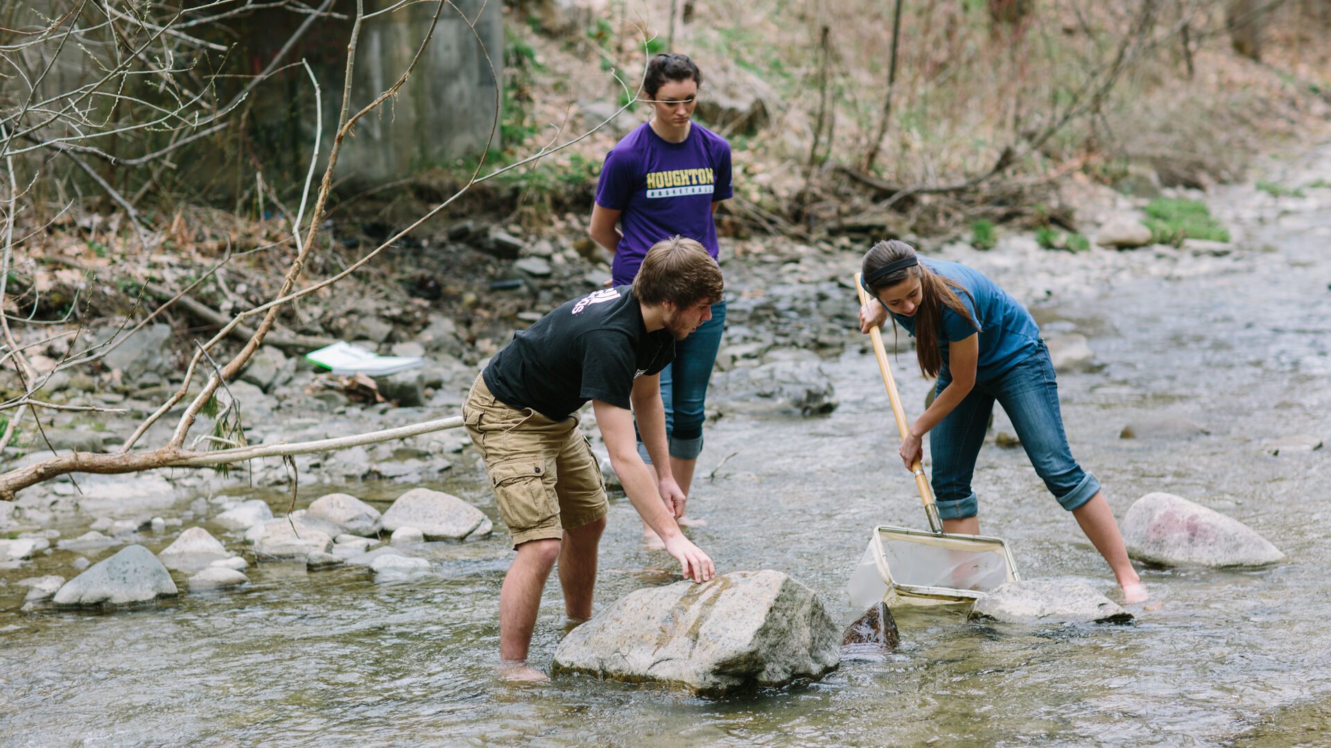 Three Houghton environmental biology students using nets in local stream.