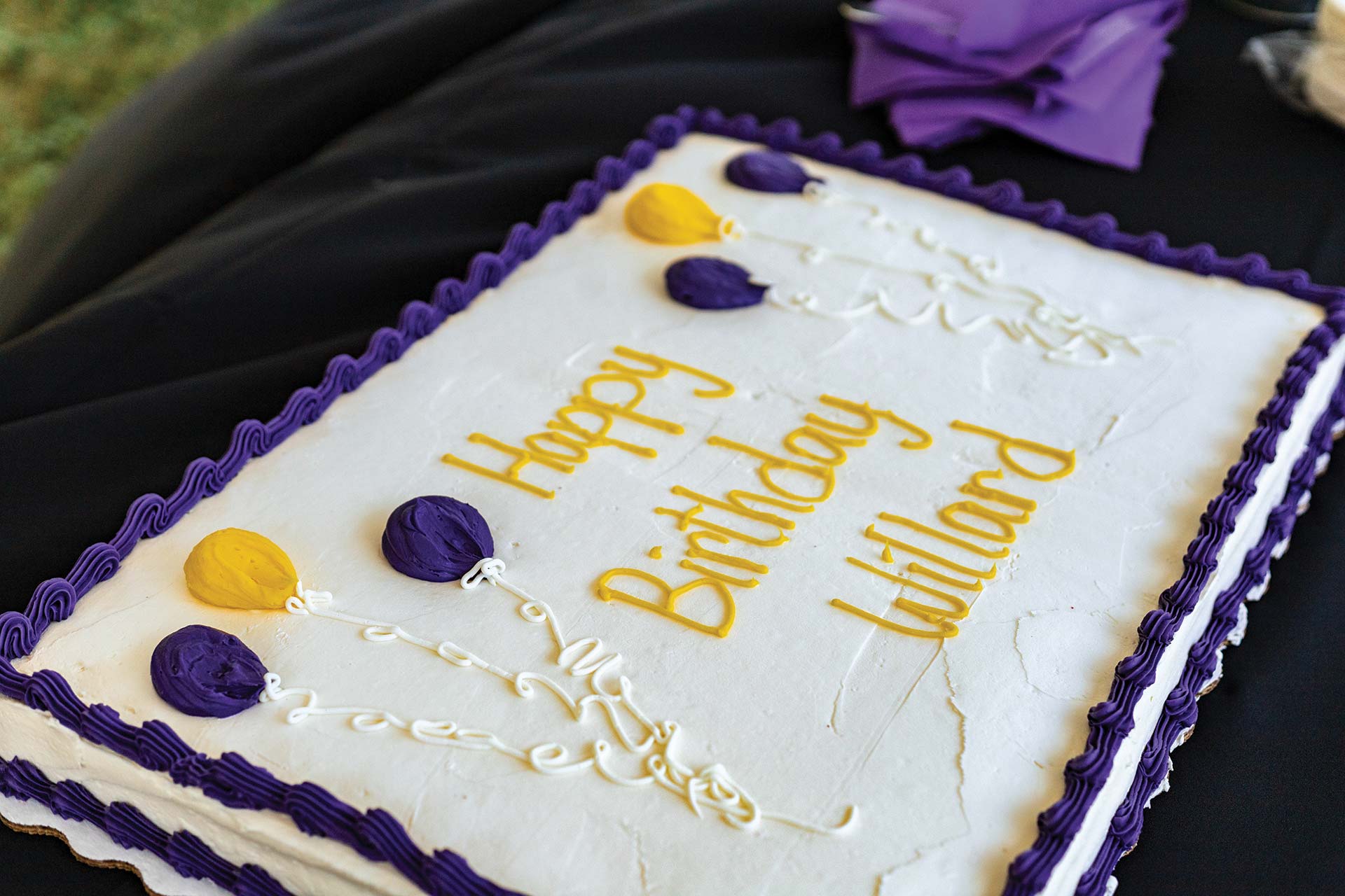 Celebration cake in white, gold, and purple that says Happy Birthday Willard.