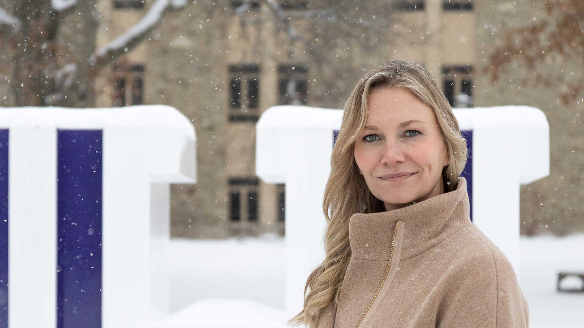 Heather Arnold standing outside in the snow on Houghton's campus wearing a tan coat.
