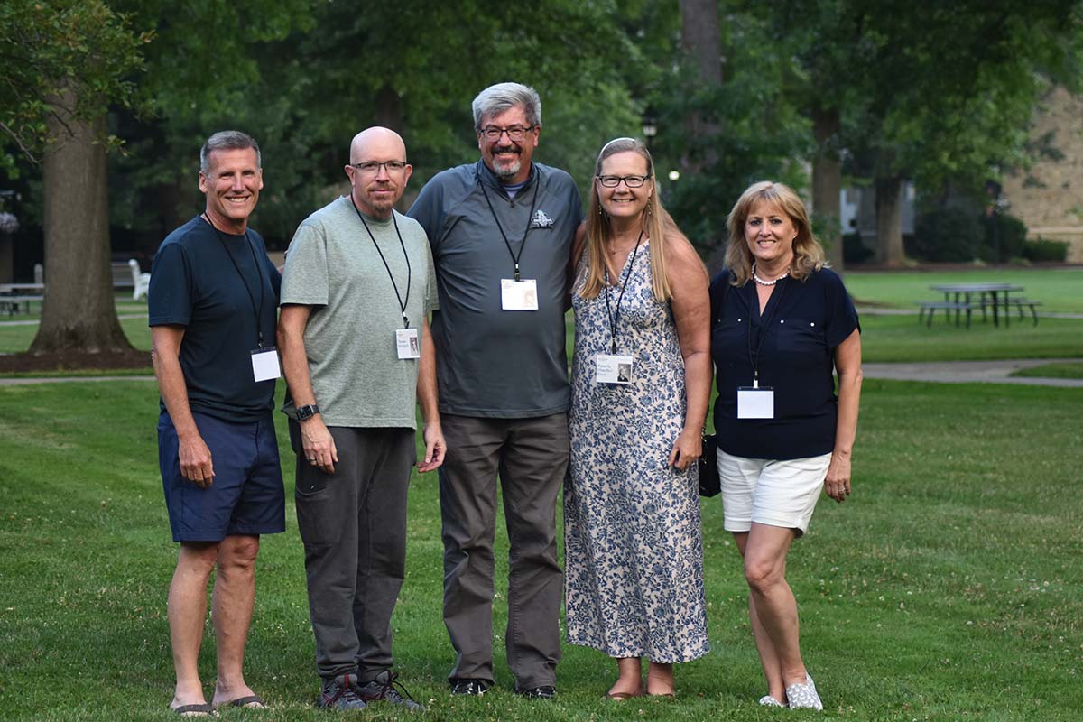 Group of five alumni standing on campus lawn at class reunion.