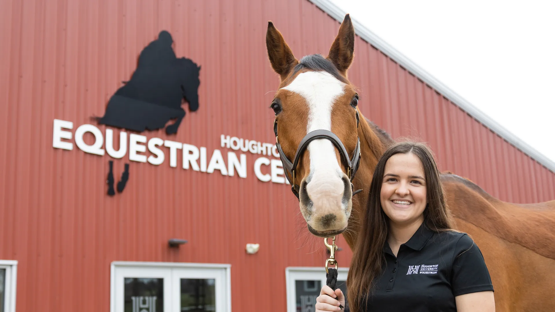 ���Ͽ� equestrian studies student Cassidy Kuhlmann standing with horse in front of equestrian center.