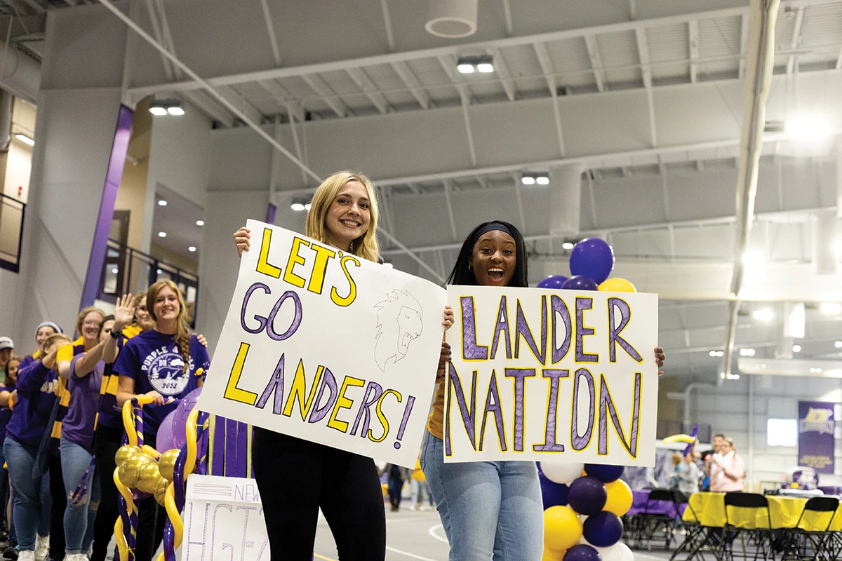 Two Houghton students holding up purple and gold signs during Homecoming.
