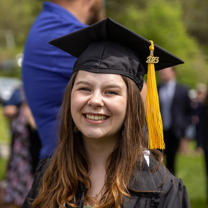 Houghton graduate standing smiling with cap and gown.