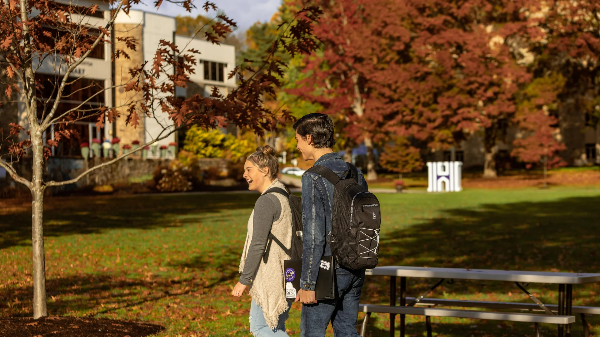Two Houghton students walking and talking on campus during the fall.