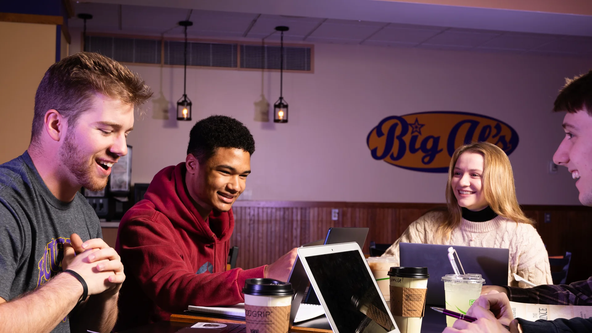 Houghton University students sitting at table visiting and working on laptops.