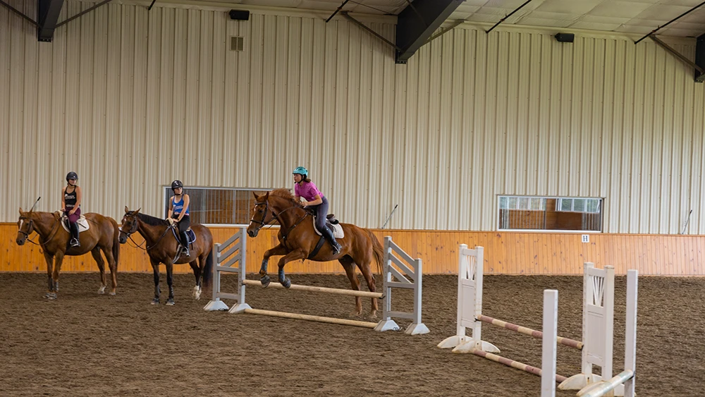 Equestrian students riding horses over jumps at indoor arena at the Equestrian Center.