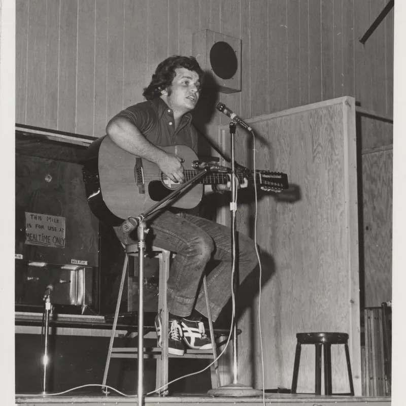 black and white photo of a 1976 male student playing the guitar on stage